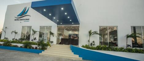 L’entrée d’un hôtel moderne, avec une façade bleue et blanche, un escalier menant à l’entrée et un espace paysager agrémenté de plantes.