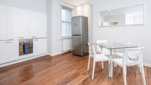 A modern kitchen with white cabinets, a stainless steel refrigerator, and a glass dining table with white chairs. - Roomspace Apartments -Sterling House (London)