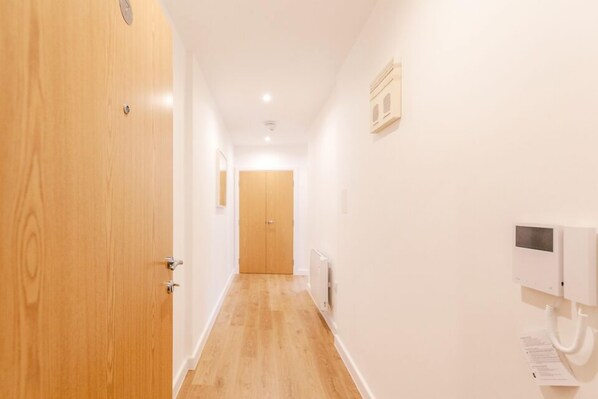 A narrow hallway with wooden flooring, white walls, and a wooden door on the left. - Roomspace Apartments -Swan House (Leatherhead)
