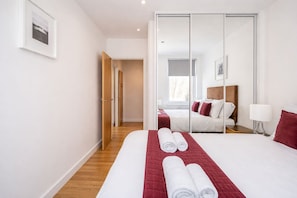 A modern hotel room with a large bed, a mirror, and a view of another room. - Roomspace Apartments -Swan House (Leatherhead)