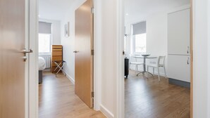 A modern apartment with a wooden floor, a dining area with a small table and chairs, and a bedroom with a bed and a wooden wardrobe. - Roomspace Apartments -Swan House (Leatherhead)