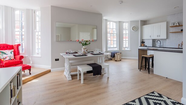 A modern kitchen with white cabinetry, a dining area with a white table set for four, and a red armchair. - Californication (Southend-on-Sea)
