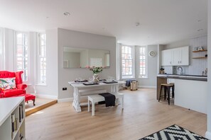 Une cuisine moderne avec des meubles blancs, un coin repas doté d’une table blanche pour quatre personnes et un fauteuil rouge.
