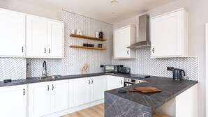 A modern kitchen with white cabinets, a herringbone-patterned backsplash, and a marble countertop. - Californication (Southend-on-Sea)