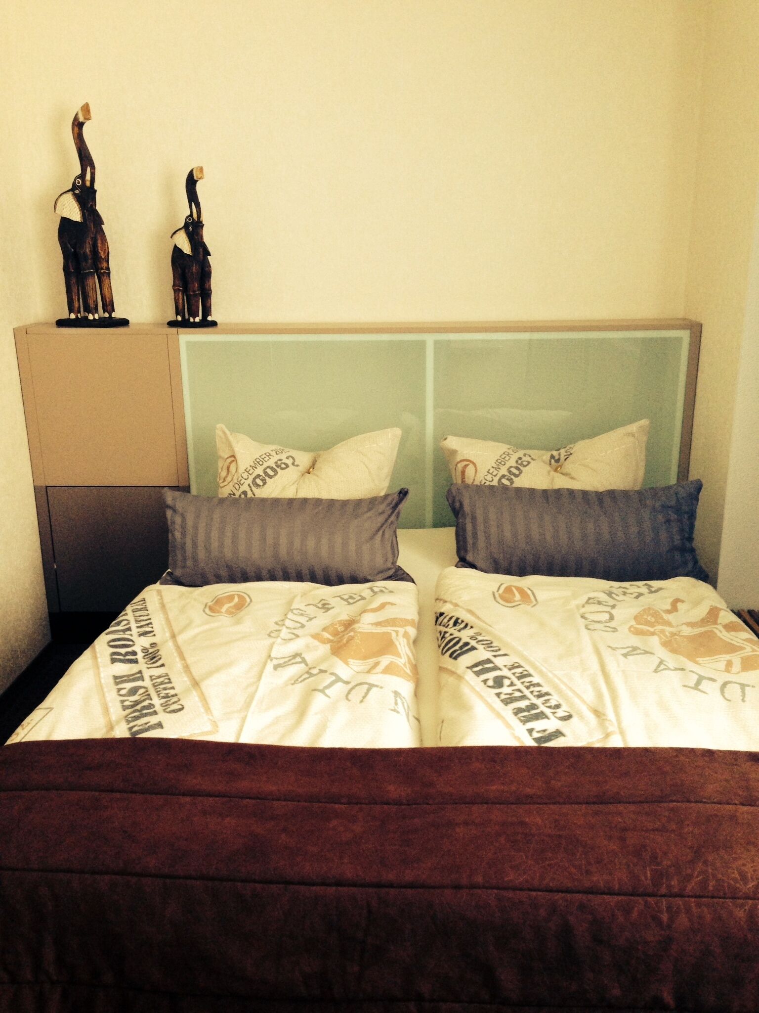 Ein Doppelbett mit braunem Kopfteil, zwei Kissen und einer dekorativen Holzfigur darauf.