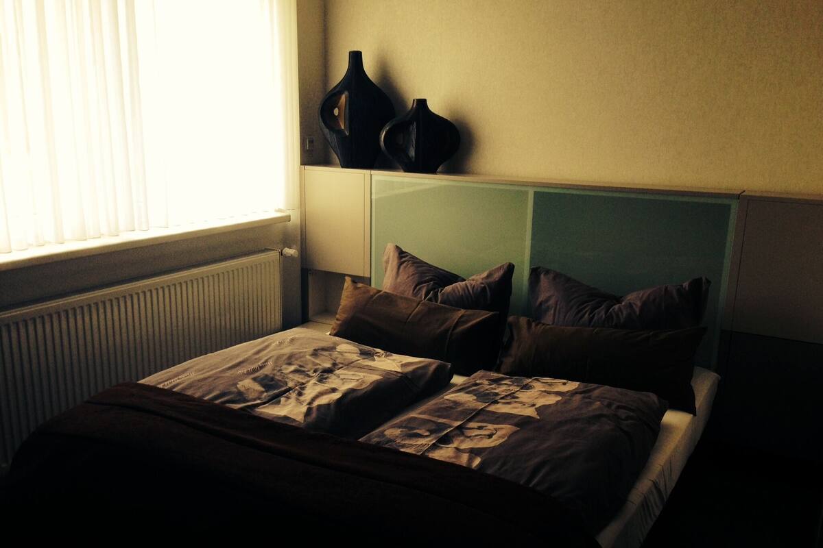 Ein Schlafzimmer mit einem Bett, Kissen und zwei Vasen auf einem Regal.