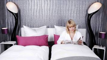 Une chambre d’hôtel avec deux lits, chacun étant équipé de draps blancs et d’oreillers roses. Il y a deux tables de chevet avec des lampes.