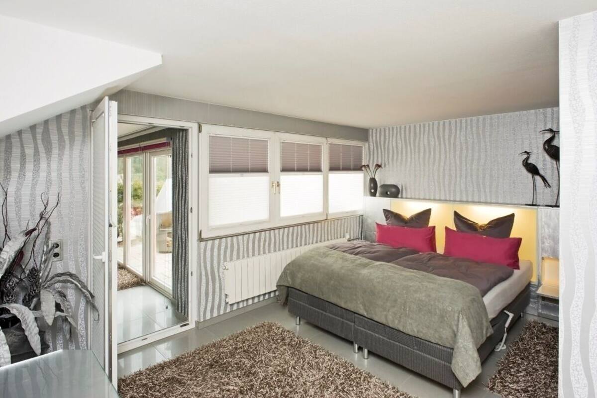 Ein modernes Schlafzimmer mit einem Bett, einem Fenster und einer Tür zu einem Außenbereich.