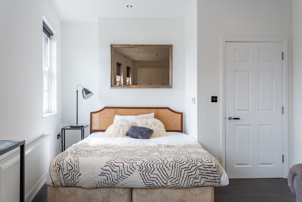 Een slaapkamer met een bed, een bedlamp, een spiegel en een deur.