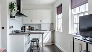 A modern kitchen with white cabinets, a black stove, and a large window with a view. - Namastay in Bed (Southend-on-Sea)