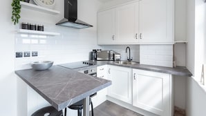 A modern kitchen with white cabinets, a marble countertop, a black range hood, and a sink. - Namastay in Bed (Southend-on-Sea)
