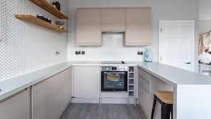 A modern kitchen with built-in appliances, wooden shelves, and a herringbone-patterned backsplash. - Exhale (Southend-on-Sea)