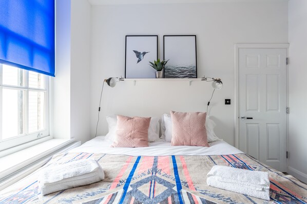 Relax in a serene bedroom with a large bed, framed artwork, and a potted plant.