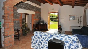 Quarto com cama, televisão, escrivaninha e vista para um jardim através de uma porta aberta.