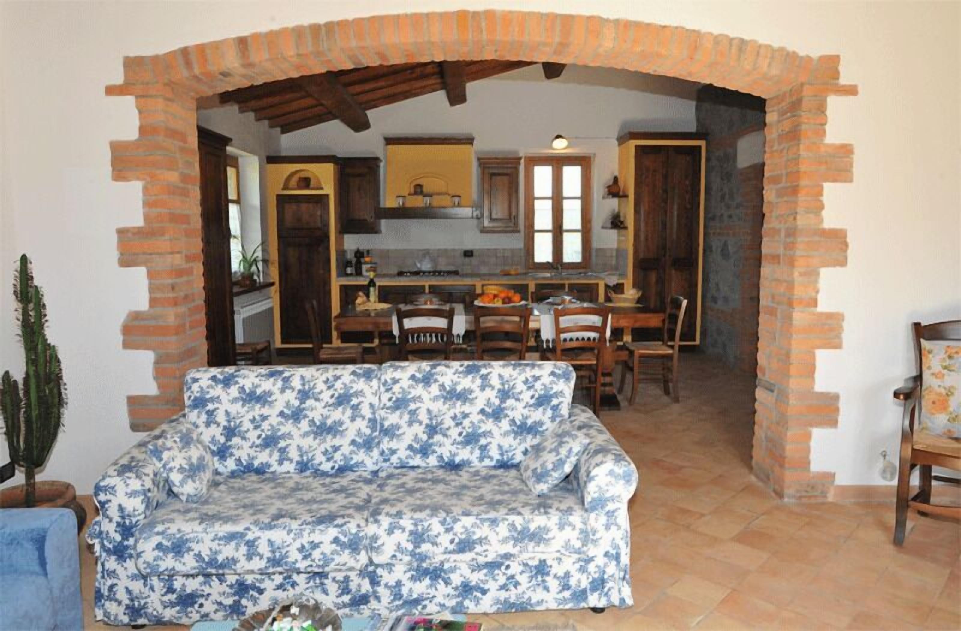 A living room with a blue floral sofa, a cactus, and a dining area with wooden chairs and a table.