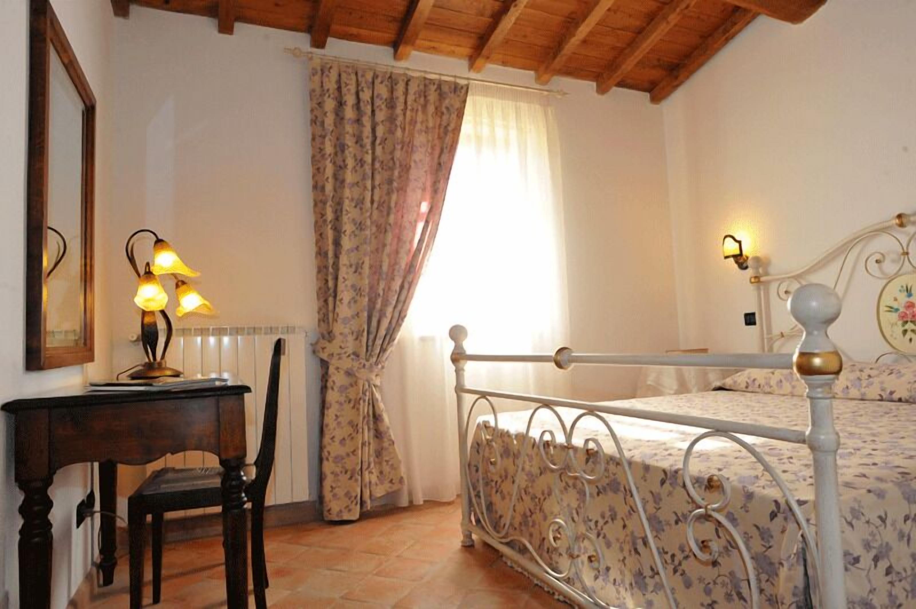 A bedroom with a bed, a desk with a lamp, a chair, and a window with curtains.