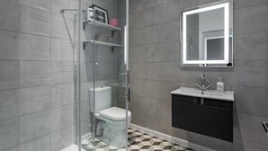 Une salle de bain moderne avec une douche à parois de verre, des toilettes blanches, un lavabo noir avec un miroir au-dessus, et un sol carrelé avec un motif géométrique.