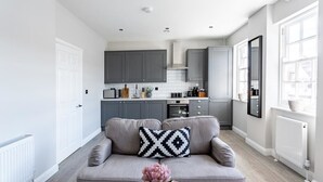 Une cuisine moderne avec des meubles gris, un canapé gris agrémenté d’un coussin noir et blanc, et un vase de fleurs.