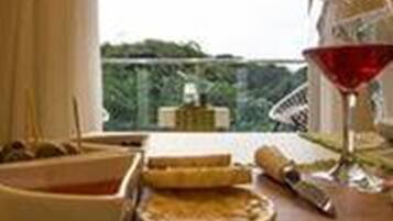 Una mesa con un bol, un plato con comida, un vaso de líquido rojo y un objeto enrollado, posiblemente una servilleta o un menú, con vistas a la vegetación exterior.