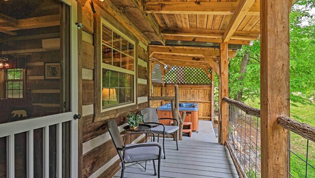 A wooden deck with a table and chairs, a hot tub, and a view of the surrounding greenery. - Covered Deck & Fire Pit: Smoky Mountain Cabin (Cosby)