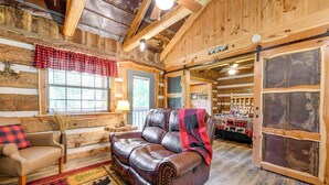 A cozy cabin interior with a leather sofa, a wooden bench, and a rustic wooden floor. - Covered Deck & Fire Pit: Smoky Mountain Cabin (Cosby)