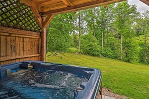 Ein Whirlpool unter einer Holzpergola mit Blick auf eine Wiese und Bäume.