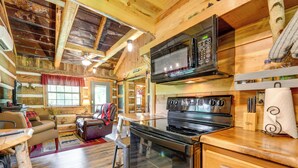 A rustic kitchen with a modern stove, microwave, and wooden cabinetry. - Covered Deck & Fire Pit: Smoky Mountain Cabin (Cosby)