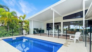 Ein moderner Poolbereich im Freien mit einem klaren, blauen Pool, weißen Liegestühlen und einer überdachten Terrasse.