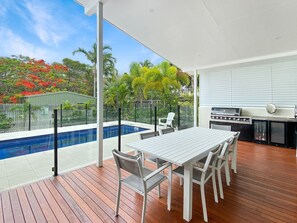 Un espacio al aire libre cubierto con piscina, mesa de comedor, sillas y una parrilla.