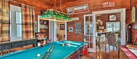 A pool table with cues and balls, wooden walls, and a plaid curtain.