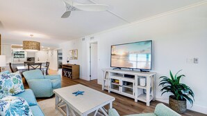 Un salon moderne doté d’un téléviseur à écran plat, d’un ventilateur de plafond et d’un coin repas avec une table et des chaises.