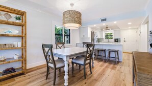 Une cuisine moderne avec des meubles blancs, un îlot central et un coin repas comprenant une table blanche et des chaises en bois.