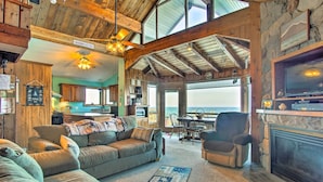 A cozy living room with a fireplace, a large sofa, and a dining area with a view of the ocean. - Lakefront Montague Cottage w/ Deck & Beach! (Montague)