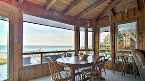 A wooden cabin with a round dining table and chairs, large windows overlooking the ocean, and a colorful rug on the floor. - Lakefront Montague Cottage w/ Deck & Beach! (Montague)