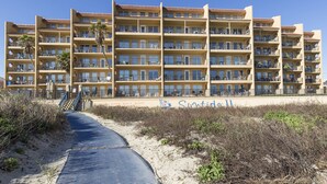A multi-story hotel with balconies, a sandy beach in front, and a clear blue sky. - Suntide II 401 - Beachfront Direct Ocean Views, Private Balcony, Heated Pool, Hot Tub, Beach Access, Walking distance to Dining and Shopping (South Padre Island)