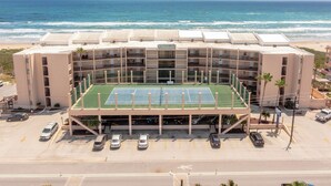 A multi-story hotel with a tennis court, parking area, and ocean view. - Suntide II 401 - Beachfront Direct Ocean Views, Private Balcony, Heated Pool, Hot Tub, Beach Access, Walking distance to Dining and Shopping (South Padre Island)