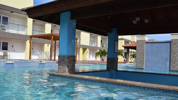 A swimming pool with clear water, surrounded by a covered area with wooden beams and stone pillars. - Bright Condo steps to Eagle Beach (Oranjestad-West)