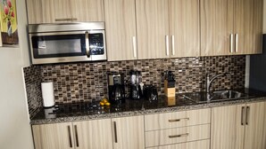 A kitchen with wooden cabinets, a stainless steel microwave, a coffee maker, and a sink. - Bright Condo steps to Eagle Beach (Oranjestad-West)