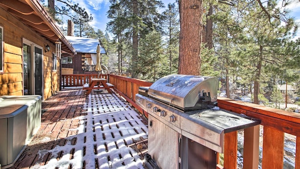 A wooden deck with a grill and a covered seating area, surrounded by tall pine trees. - Walk to Lake: Rustic Home w/ Deck in Fawnskin (Fawnskin)