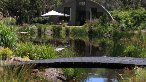 A modern house with a curved roof, a dining area with outdoor furniture, and a pond in the foreground. - Glenlowren - A magical haven in the Yarra Valley (Dixons Creek)