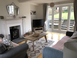 A living room with a fireplace, a television, and a large window with a view of the garden.