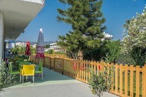 An outdoor seating area with tables and chairs, a wooden fence, and a large tree.