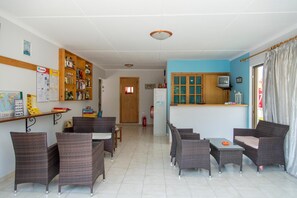 A room with wicker furniture, a wooden shelf with various items, a small television, and a door leading to another room. - Yannis Yard Studios And Apartments (Kos)