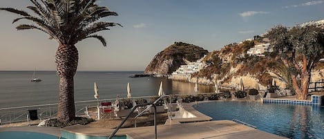 Zona de piscina con vista al mar, una palmera y montañas al fondo.