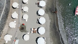 An aerial view of a beach with rows of umbrellas and lounge chairs, a stone wall, and a clear view of the ocean. - Apollon Club (Serrara Fontana)