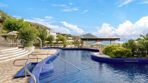 A swimming pool with steps and lounge chairs, surrounded by greenery and a mountain in the background. - Apollon Club (Serrara Fontana)