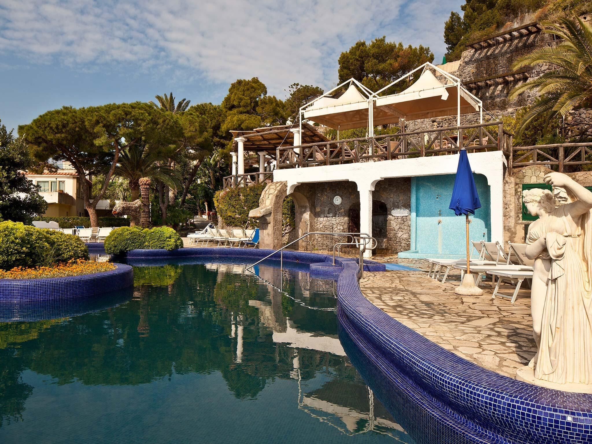 A pool area with a stone wall, lounge chairs, and a statue.