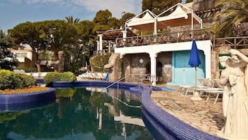 A pool area with a stone wall, lounge chairs, and a statue.