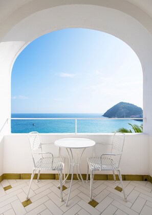 A balcony with two white metal chairs and a small white table, overlooking a clear blue sea and a distant island. - Apollon Club (Serrara Fontana)