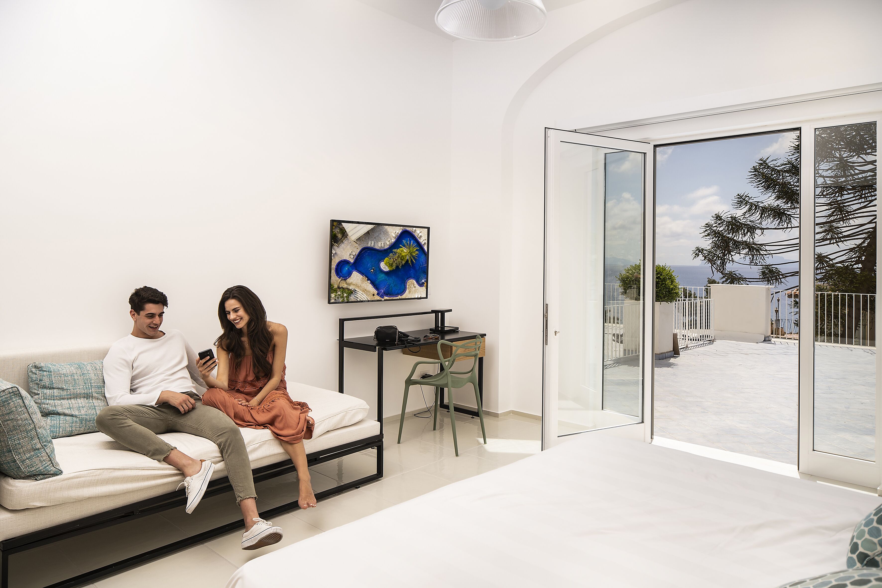 A modern bedroom with a bed, a desk, and a large sliding glass door leading to a balcony.